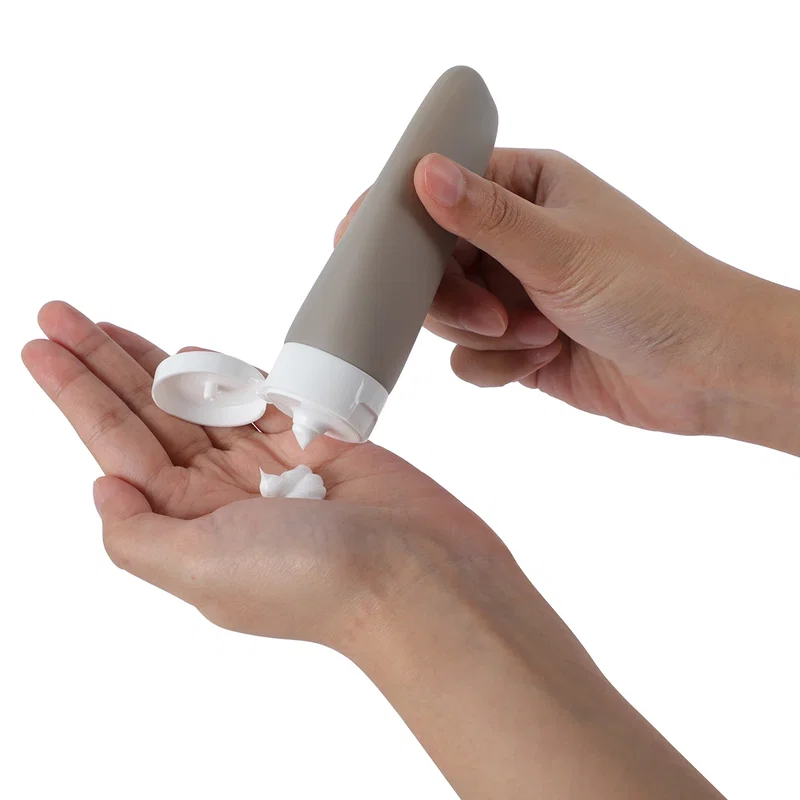 Continental travel bottle in taupe gray dispensing lotion into a hand, in-use shot