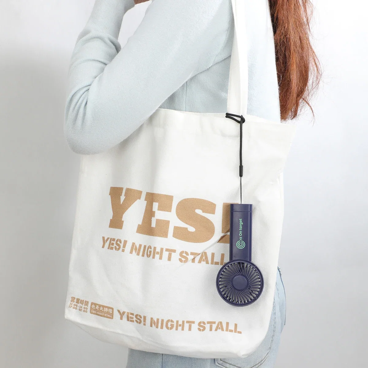 Easy Breeze hand fan's lanyard looped around a tote bag strap, lifestyle carry shot